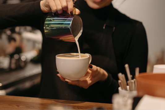 mujer sirviendo taza de café con leche en la barra de una cafeteria