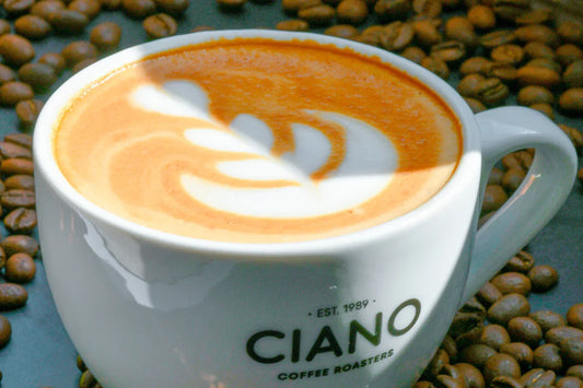 taza de ciano coffee con café espresso con un latte art sobre una mesa con granos de café